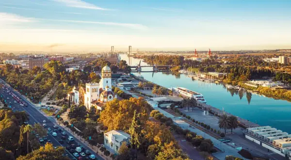 Vue aérienne de Séville au coucher du soleil, avec le Guadalquivir et des bâtiments historiques. Imaginez les coureurs du marathon de Séville 2026 traversant ce paysage.