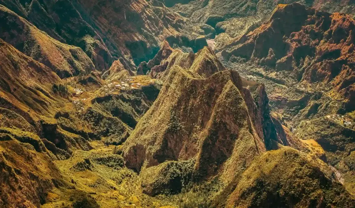Paysage spectaculaire de montagnes verdoyantes et escarpées, rappelant les défis de la diagonale des fous. Des villages sont nichés dans les vallées.