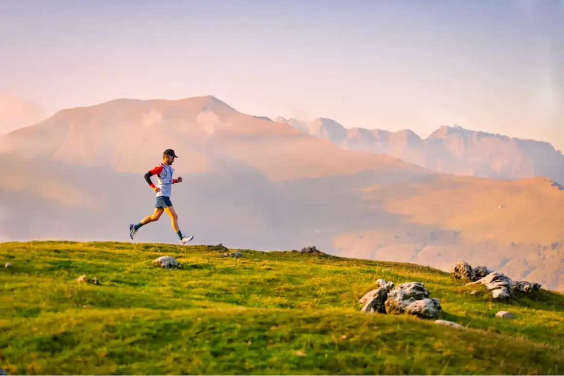 Un coureur en plein effort sur une crête herbeuse, avec des montagnes brumeuses en arrière-plan. Il participe au **championnat du monde de trail long**.