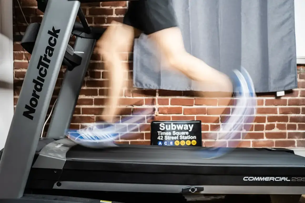 Person en mouvement sur un tapis roulant NordicTrack, simulant des gammes athlétiques. Un panneau "Subway Times Square" est visible.