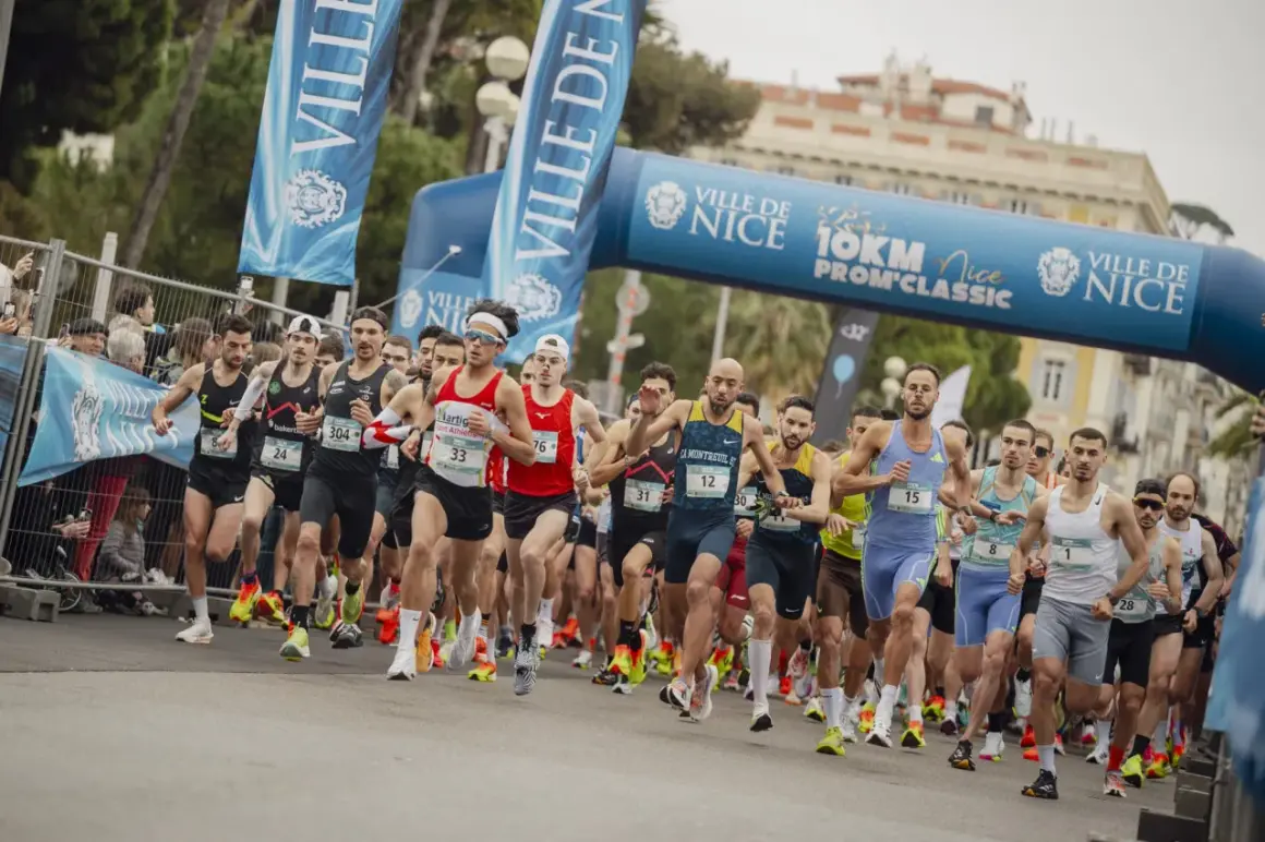 Des coureurs s'élancent sous une arche bleue lors du semi-marathon de Nice. Les numéros de dossard sont visibles.
