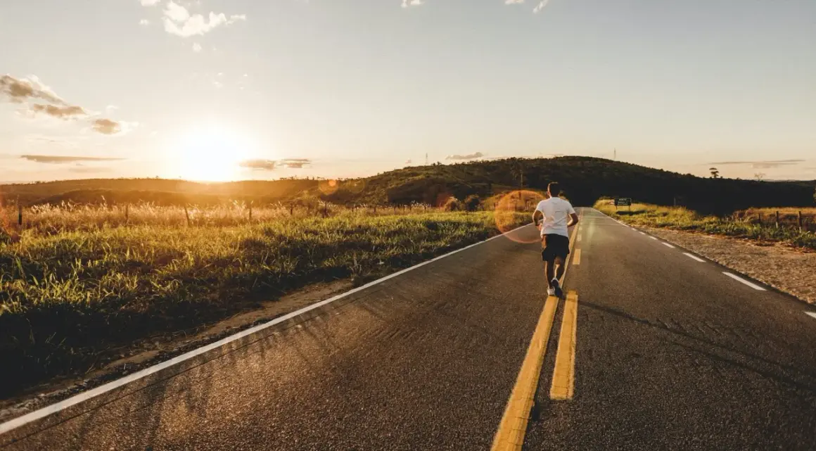 Un homme court sur un **road run trail** au coucher du soleil, profitant de la nature et de la lumière dorée.