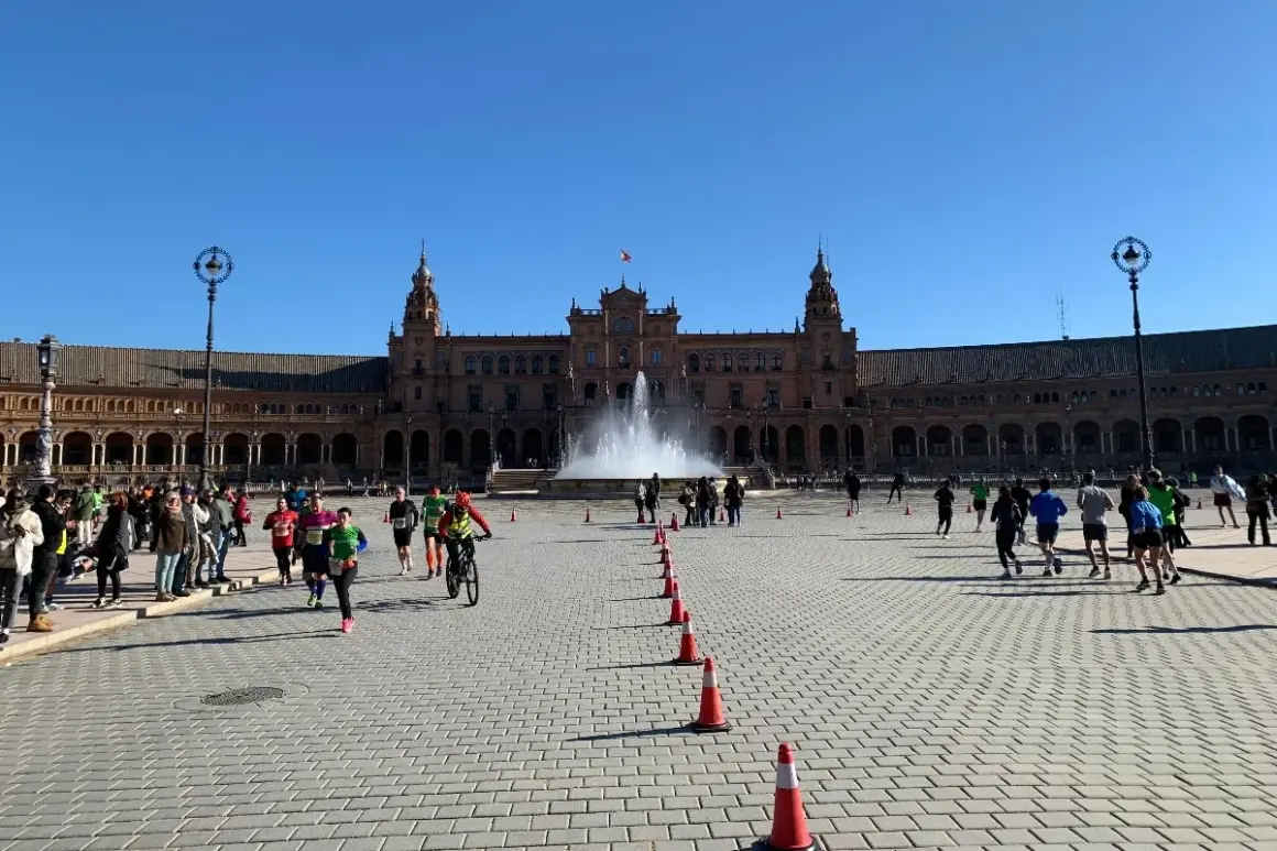Coureurs et cyclistes s'élancent sur la Plaza de España pour le semi marathon de Séville, sous un ciel bleu éclatant.