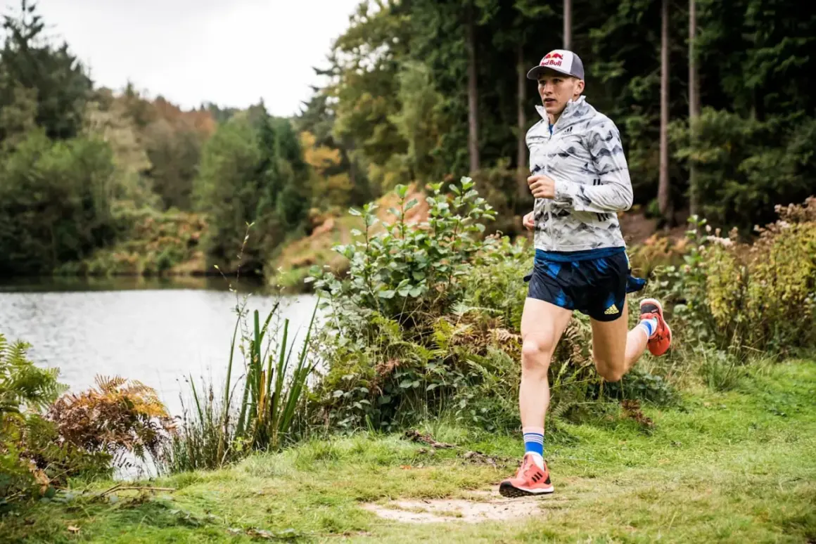 Un athlète court près d'un lac, dans une forêt. Il pourrait s'entraîner pour courir à Nantes.