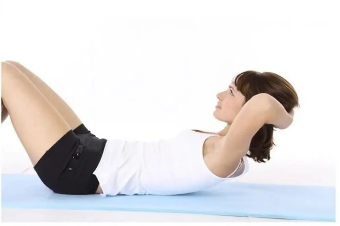 Femme effectuant des abdos hypopressifs sur un tapis bleu.