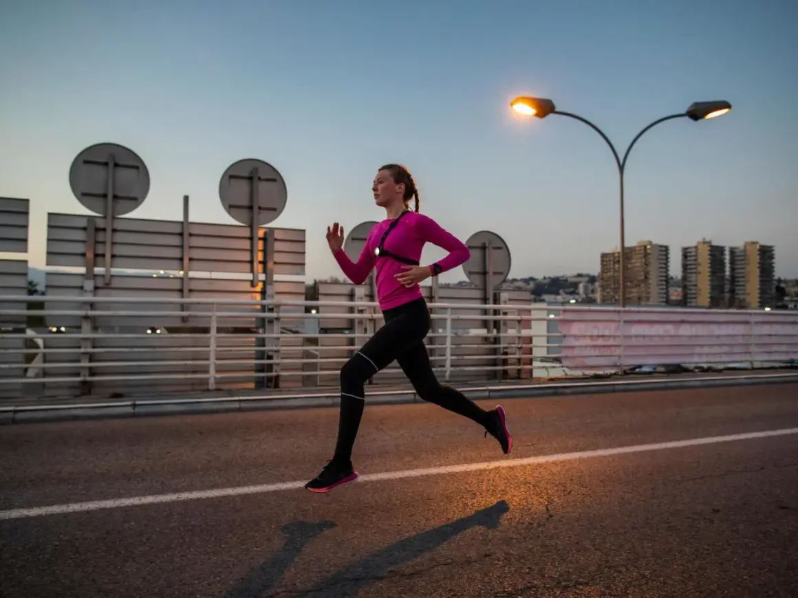 Une femme en tenue de sport rose et noire court sur une route au crépuscule, profitant d'une course de nuit sous les lampadaires.