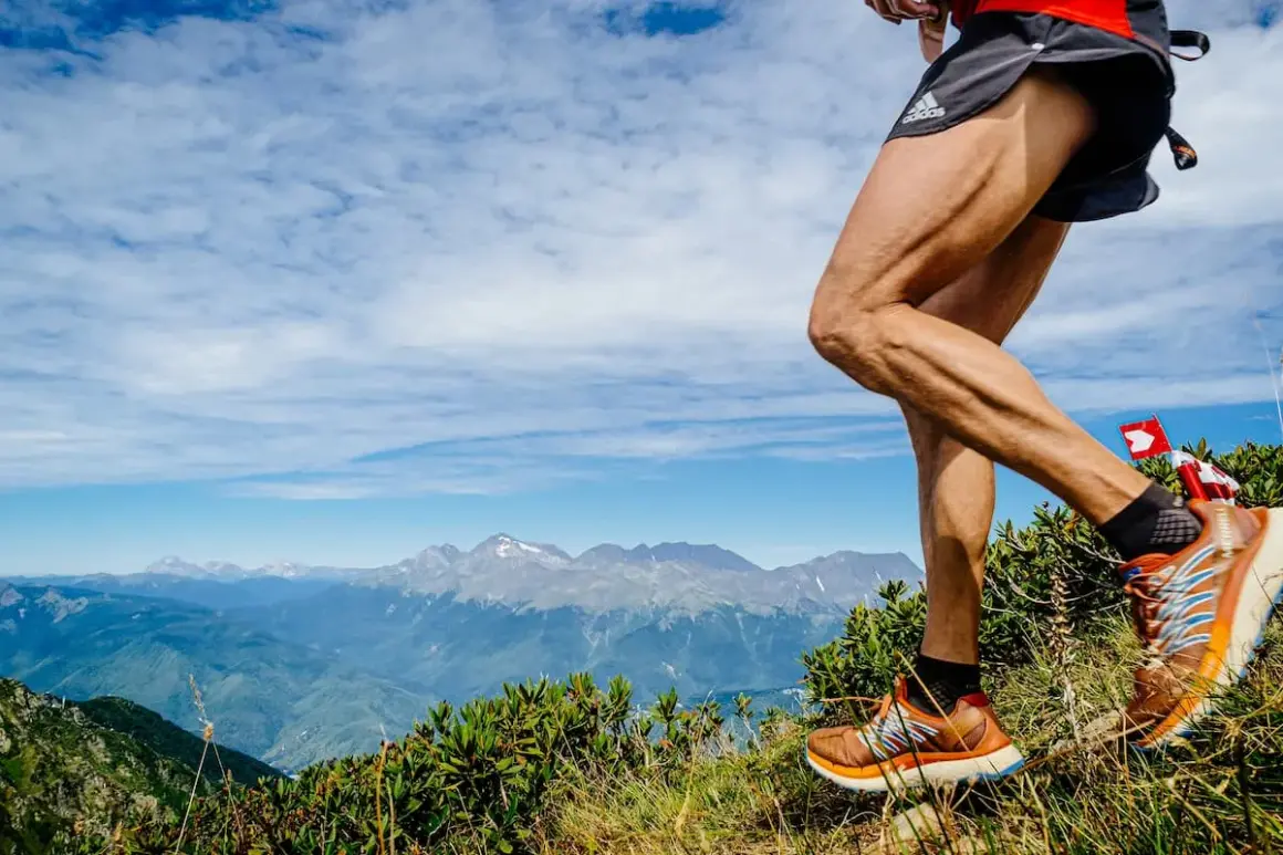 Un coureur en plein entrainement trail, jambes musclées, sur un sentier de montagne avec un panorama spectaculaire.
