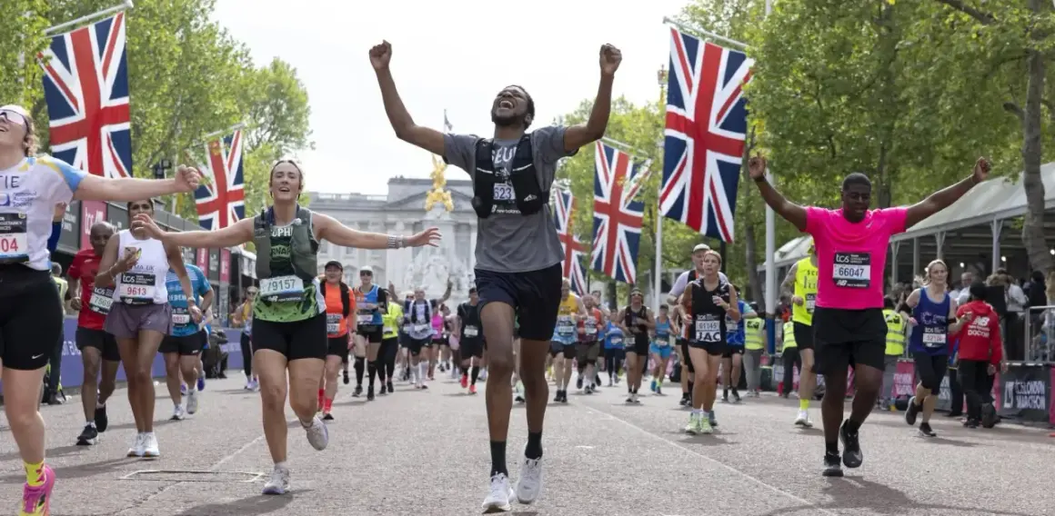 Des coureurs célèbrent leur arrivée au plus grand marathon du monde, drapeaux britanniques en arrière-plan.