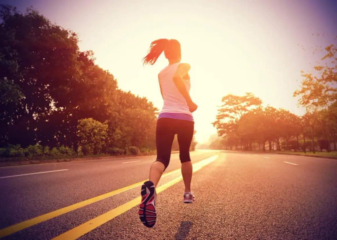 Une coureuse en plein entraînement fartlek, variant son allure sur une route bordée d'arbres au lever du soleil.