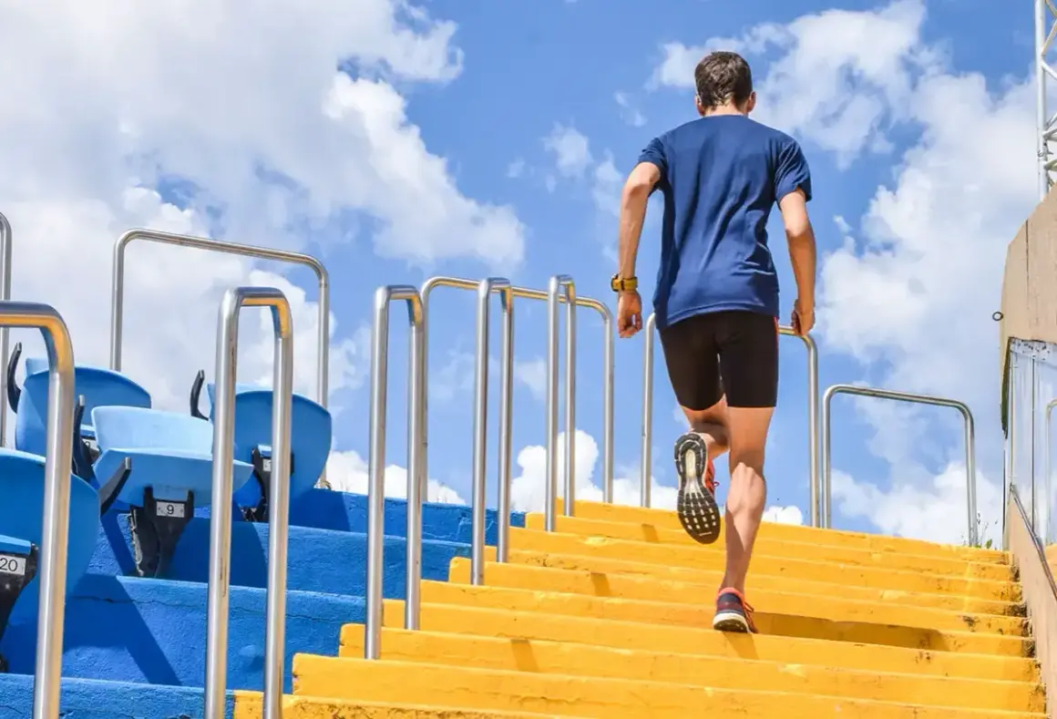 Un homme monte des marches jaunes, un entraînement efficace pour les meilleurs exercices pour les jambes. Le ciel bleu et les nuages sont visibles.
