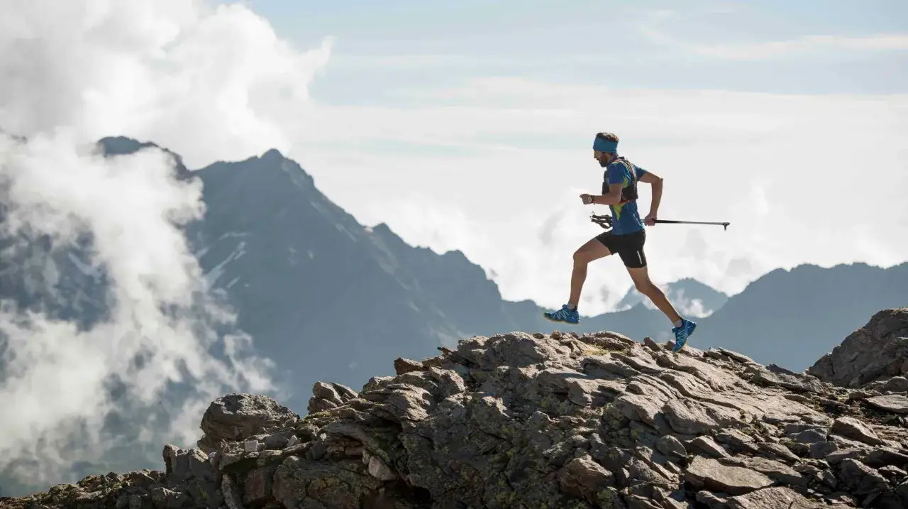 Un homme court sur un sentier rocheux en montagne, bâtons à la main. Il choisit de courir ou marcher dans ce paysage spectaculaire.