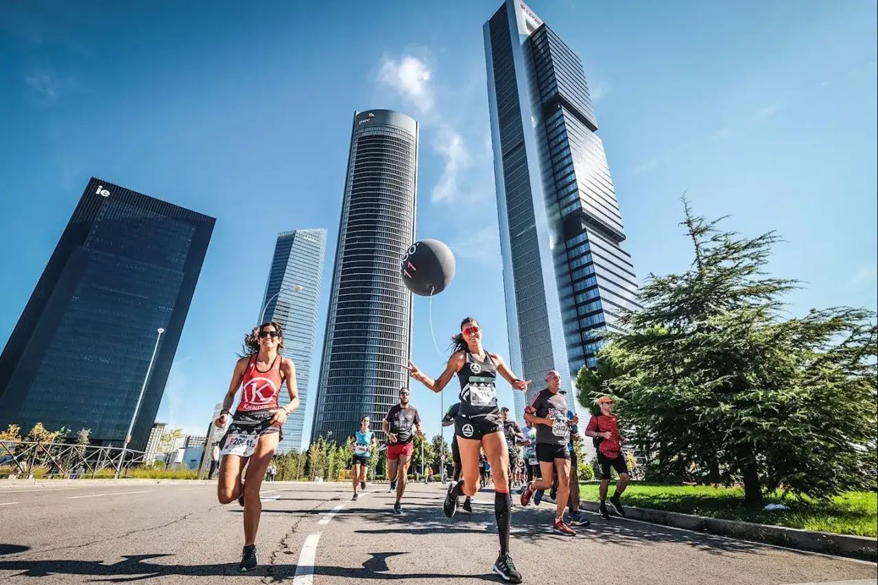 Des coureurs participent au semi marathon de Madrid, avec des gratte-ciel modernes en arrière-plan.
