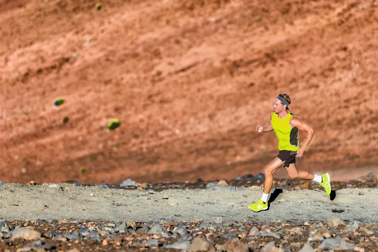 Un coureur en tenue de sport jaune et noire, concentré, s'entraîne sur un sentier rocailleux. La préparation mentale marathon est essentielle pour affronter ce défi.