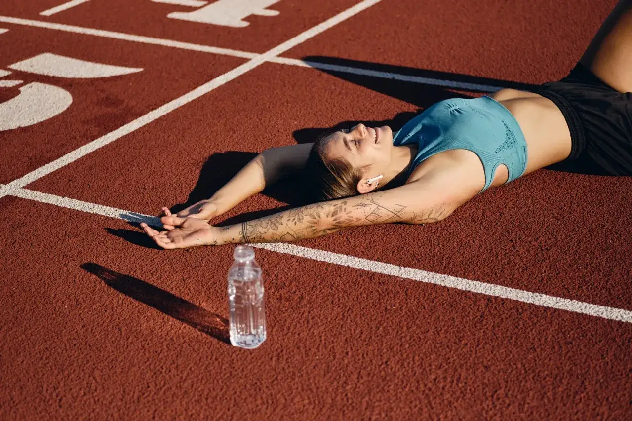 Athlète souriante, allongée sur la piste après un marathon, profitant de sa récupération. Une bouteille d'eau à ses côtés.
