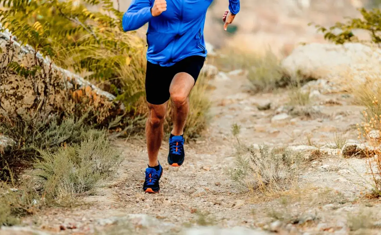 Un coureur en tenue bleue et noire s'entraîne sur un sentier rocailleux, prêt à courir avant une course.