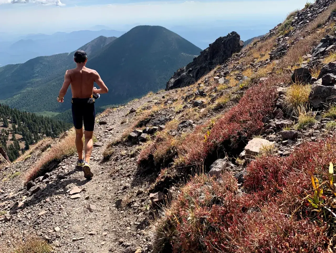 Un coureur en plein entrainement trail sur un sentier rocailleux, avec des montagnes en arrière-plan.