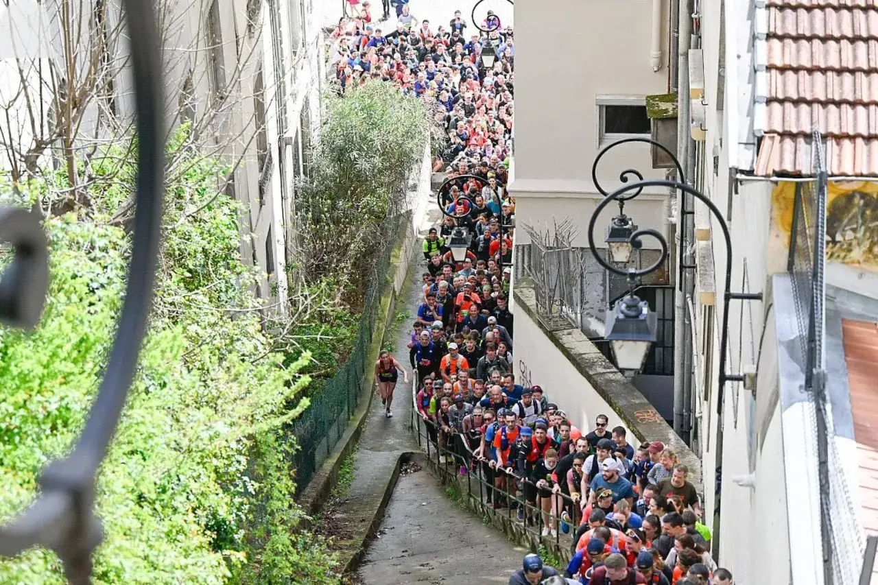 Une foule nombreuse participe à un urban trail à Lyon, dévalant une ruelle étroite bordée de végétation et de bâtiments.