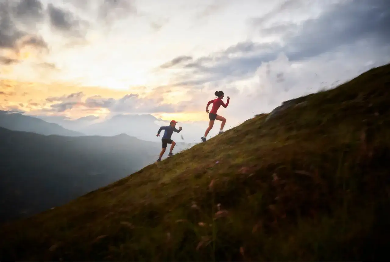 Deux coureurs s'entraînent en montagne au lever du soleil. Ils montent une pente raide, défiant l'effort. Que veut dire EF en course à pied ? C'est l'endurance fondamentale, essentielle pour de telles ascensions.
