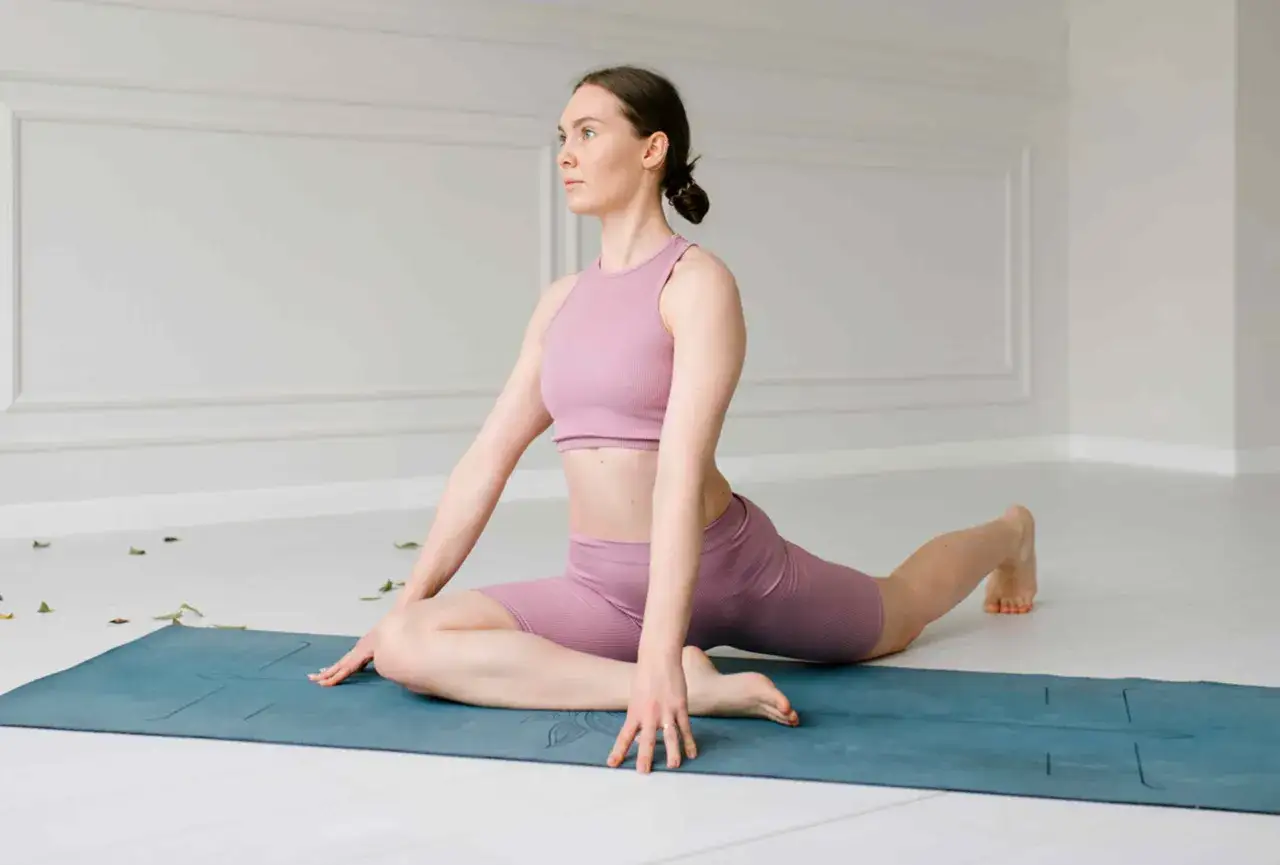 Femme en tenue de sport rose pratiquant un étirement TFL sur un tapis de yoga bleu.