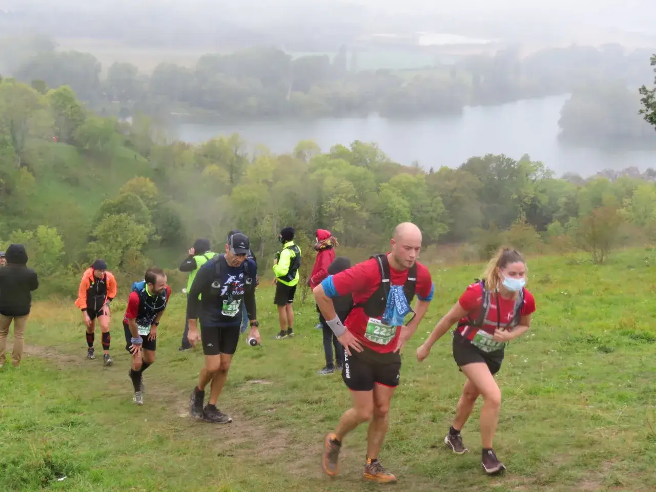 Coureurs en pleine ascension lors du trail des rois maudits, avec un lac brumeux en arrière-plan.