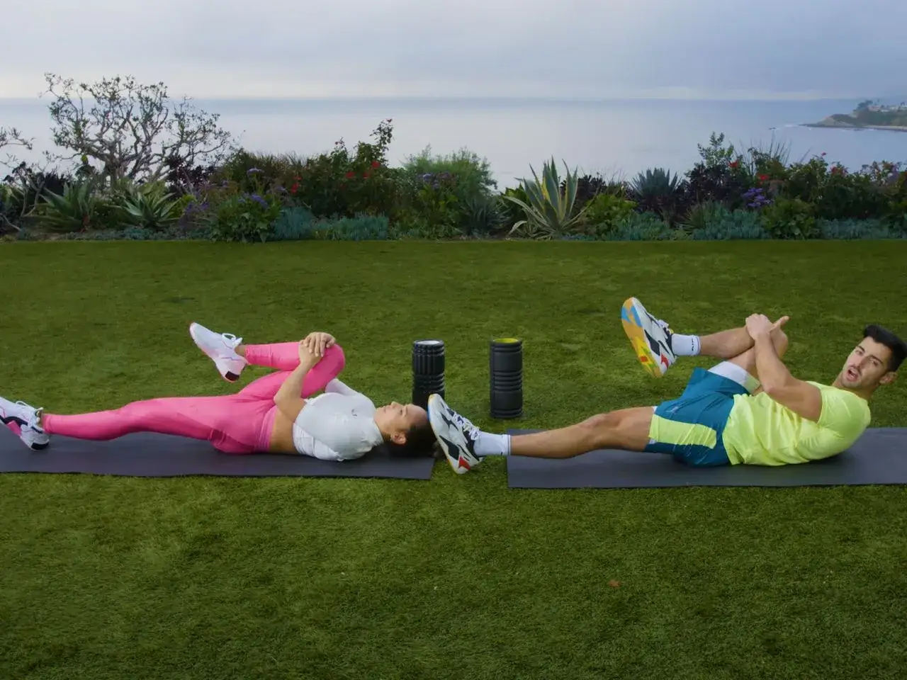 Couple faisant un exercice dos sur des tapis d'extérieur, avec vue sur l'océan.