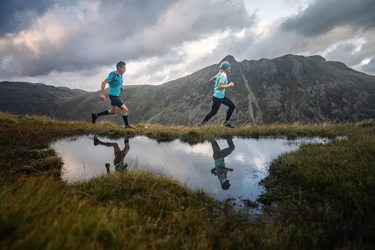 Deux coureurs profitent des bienfaits de la course &agrave; pied en pleine nature, leurs reflets dans l'eau refl&eacute;tant la beaut&eacute; du paysage montagneux.