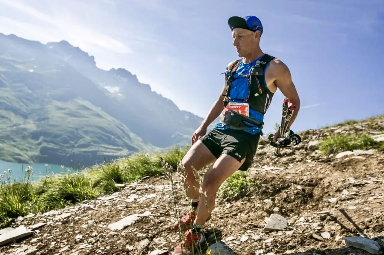 Un coureur de trail, équipé de bâtons, dévale un sentier rocailleux lors d'un course Aix-les-Bains, avec un lac et des montagnes en arrière-plan.