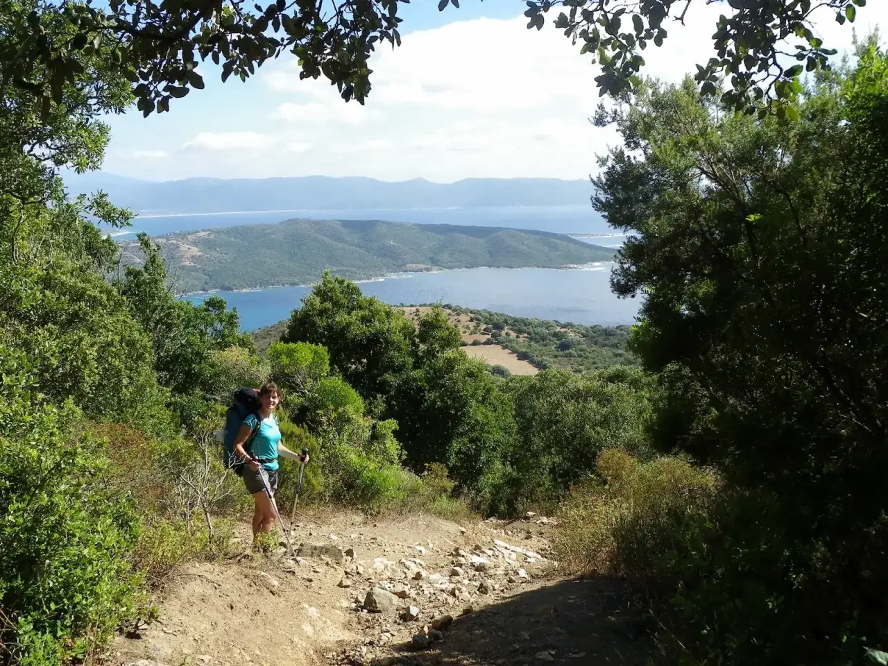Une randonneuse profite d'une vue magnifique sur la mer lors de son trail corse. Le sentier rocailleux serpente &agrave; travers la v&eacute;g&eacute;tation luxuriante.