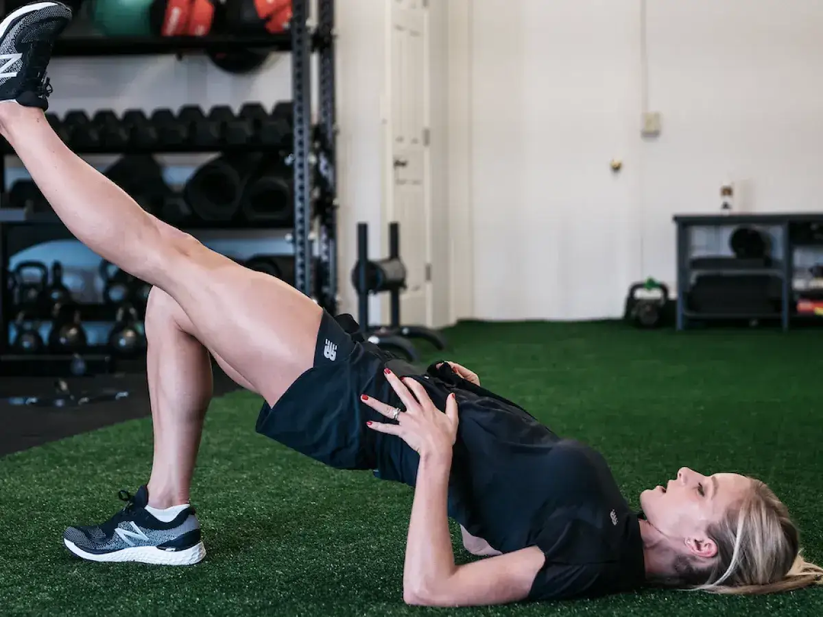 Femme effectuant un exercice de mobilité au sol, une jambe levée, dans une salle de sport.