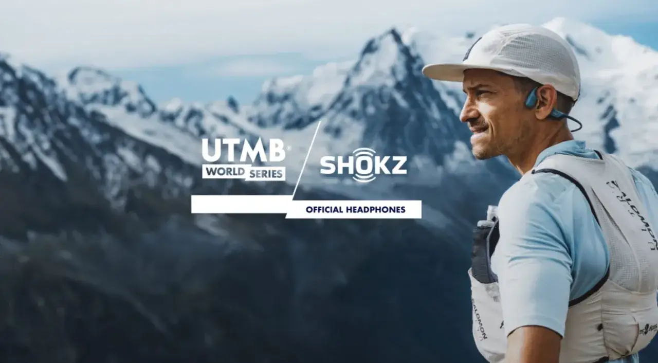 Un coureur UTMB World Series, &eacute;quip&eacute; d'&eacute;couteurs Shokz, profite du podcast trail avec un panorama de montagnes enneig&eacute;es.