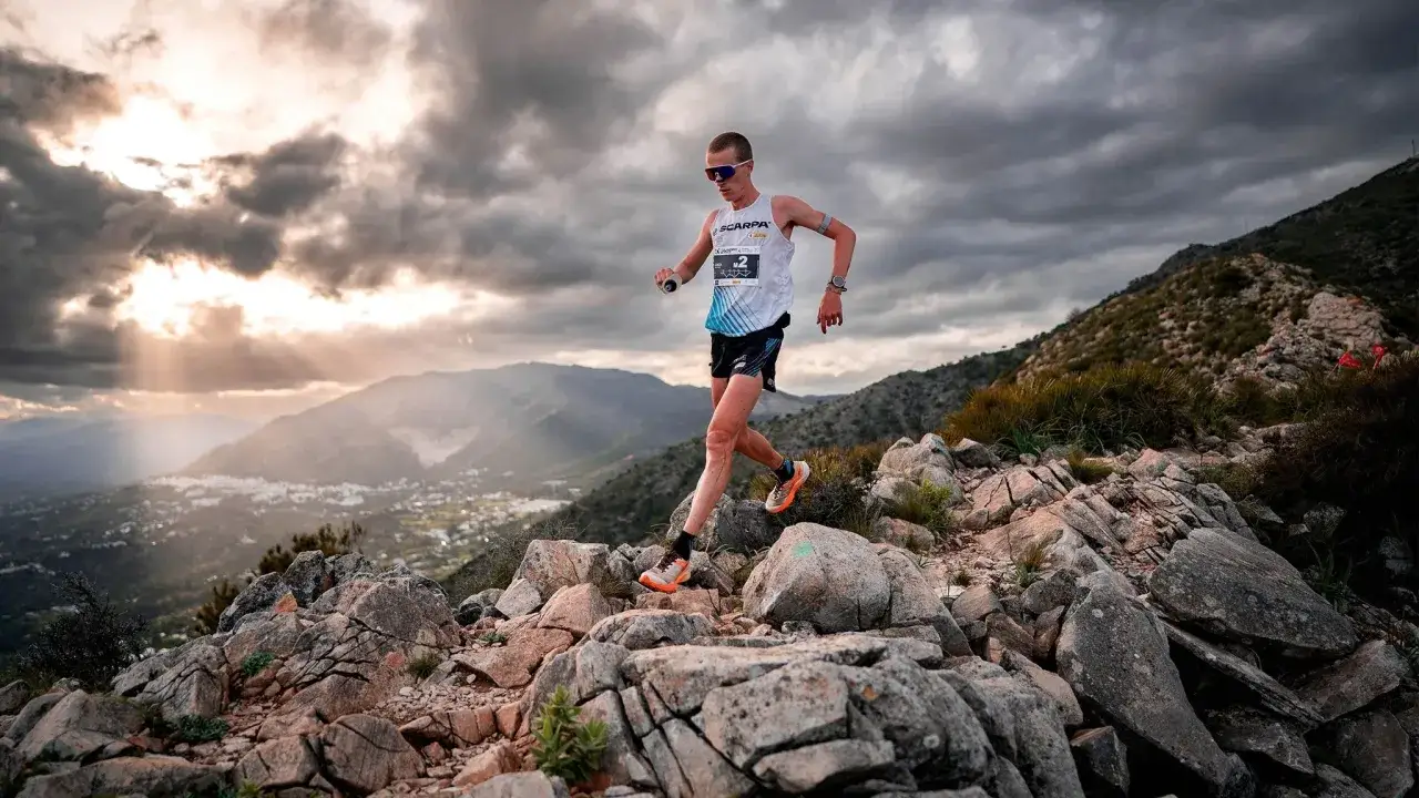 Un coureur en plein effort lors d'une sortie longue marathon, naviguant sur un sentier rocailleux avec un paysage montagneux en arrière-plan.