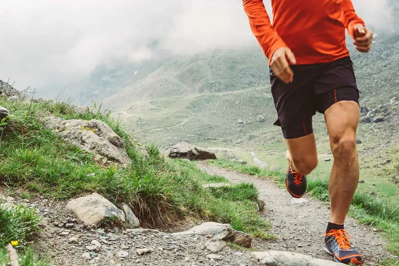 Un coureur en tenue orange et noire dévale un sentier rocailleux en montagne. Un week-end choc trail inoubliable !