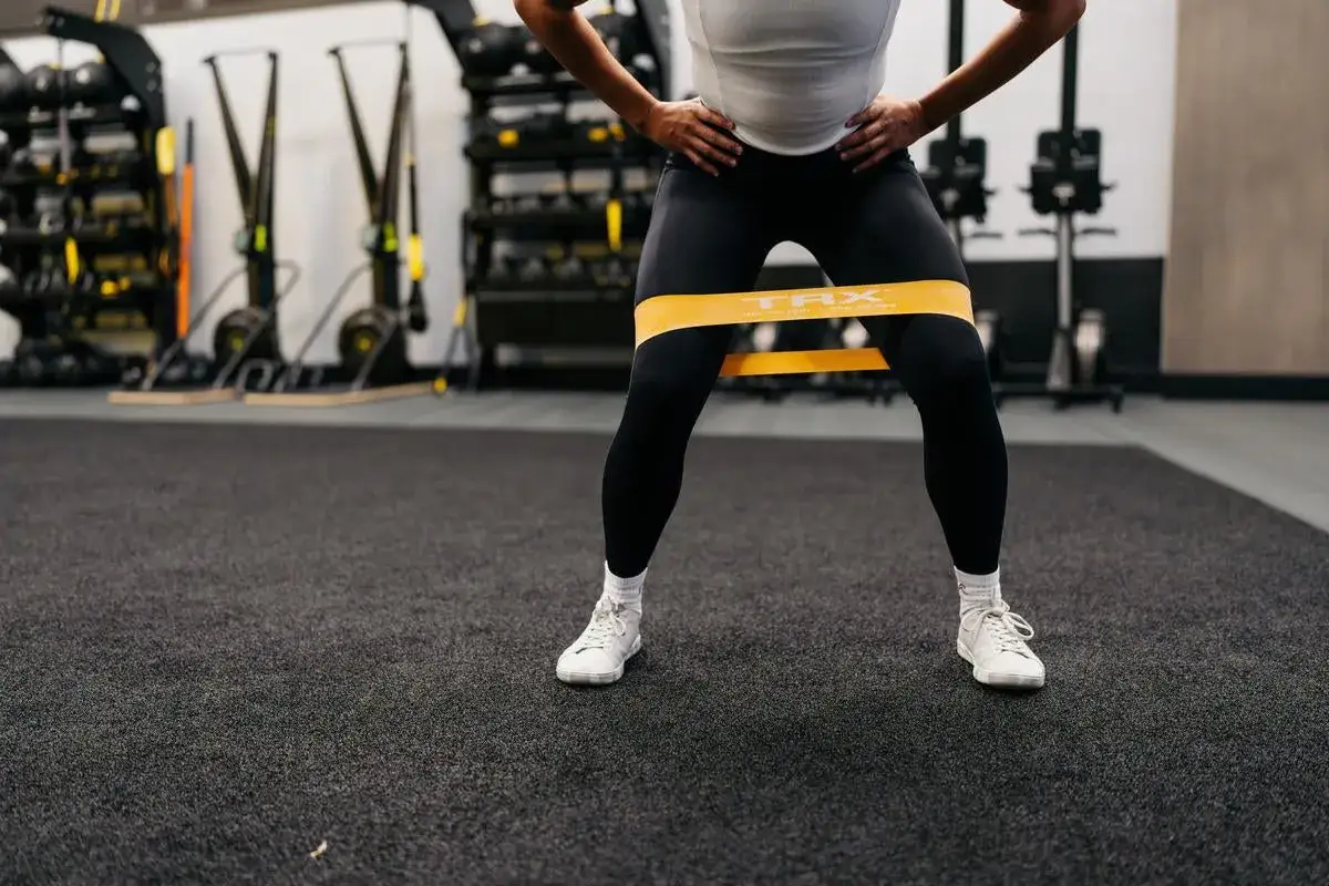 Femme effectuant un squat avec un &eacute;lastique jaune autour des cuisses pour renforcer ses muscles.