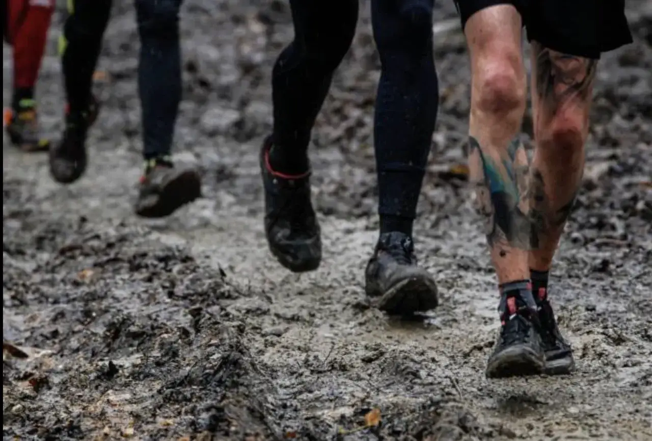 Des coureurs s'enfoncent dans la boue, déterminés à courir sous la pluie malgré le terrain difficile.