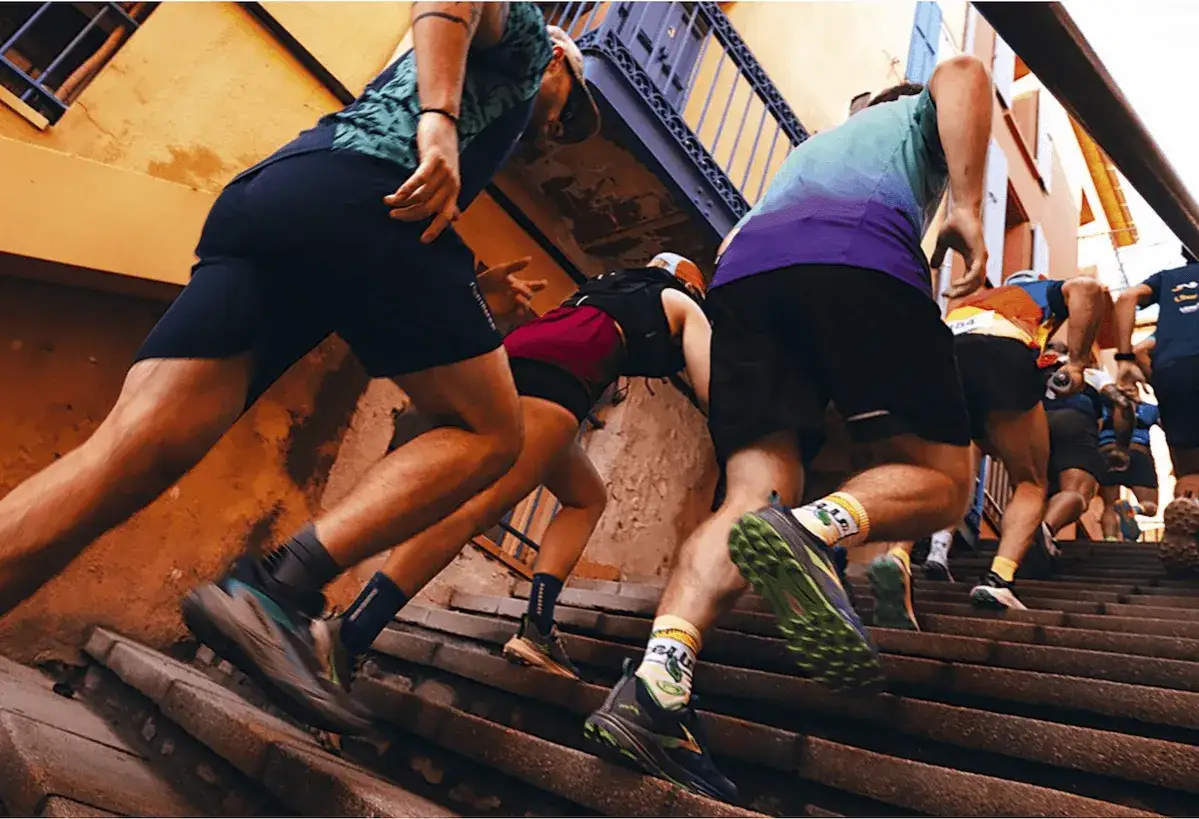 Des coureurs s'élancent dans un urban trail sur des escaliers étroits, l'effort visible sur leurs jambes musclées.