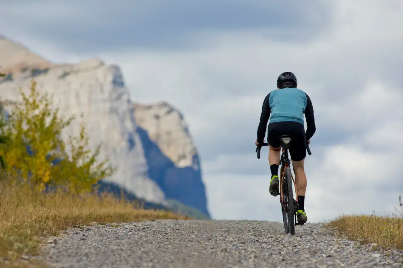 Cycliste en plein entrainement crois&eacute; sur un chemin rocailleux, face &agrave; une montagne imposante sous un ciel nuageux.