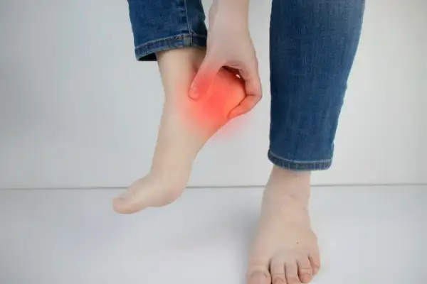 Main d'une personne touchant son talon, zone rouge indiquant une douleur. Peut-être une douleur talon course à pied.