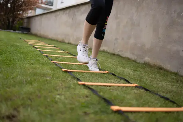 Une personne effectue un exercice lombaire sur une échelle d'agilité dans l'herbe.