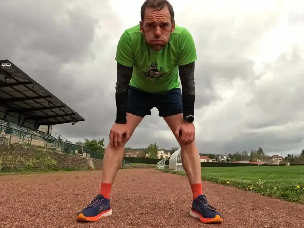 Un coureur fatigué, penché en avant sur une piste d'athlétisme, se prépare pour la récupération course à pied. Le ciel est couvert.