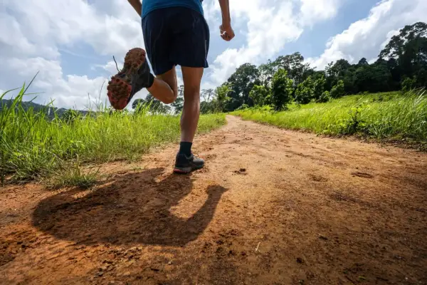 Un coureur en plein entrainement trail 20 km sur un chemin de terre bordé d'herbes hautes et d'arbres luxuriants.