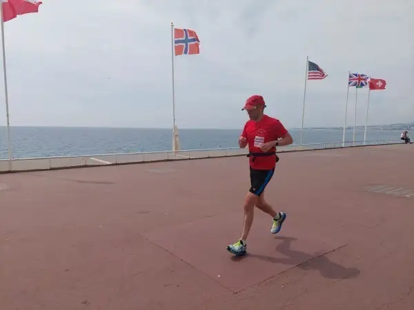 Un homme court sur la promenade des Anglais à Nice, drapeau norvégien et américain en arrière-plan.
