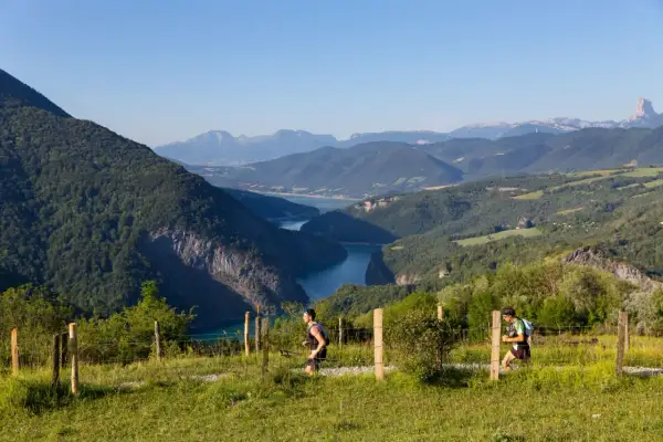 Deux coureurs s'élancent sur le sentier du maratrail des passerelles, dominant un lac bleu entouré de montagnes verdoyantes.