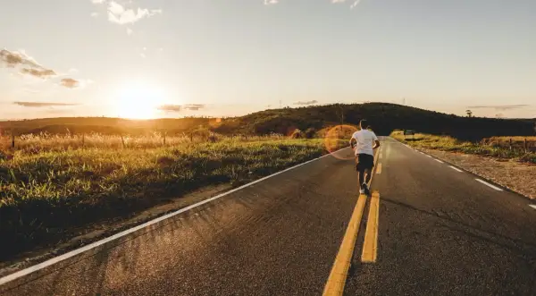 Un homme court sur un **road run trail** au coucher du soleil, profitant de la nature et de la lumière dorée.