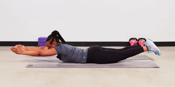 Femme effectuant un exercice abdos au sol, bras tendus devant, jambes levées.