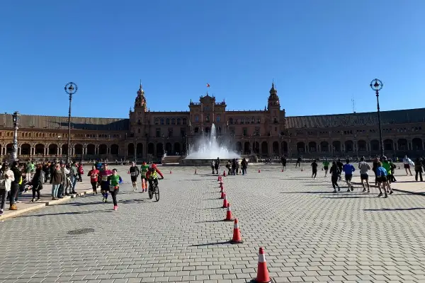 Coureurs et cyclistes s'élancent sur la Plaza de España pour le semi marathon de Séville, sous un ciel bleu éclatant.