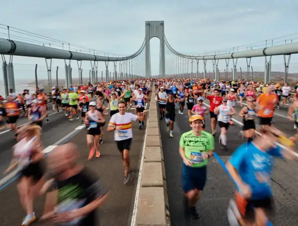 Des coureurs franchissent le pont, affrontant le dénivelé du marathon de New York. Le ciel est couvert, mais l'énergie est palpable.