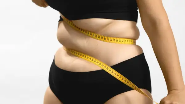 Une femme mesure son tour de taille avec un mètre ruban jaune, symbolisant le suivi du pourcentage masse grasse et le parcours de perte de poids.