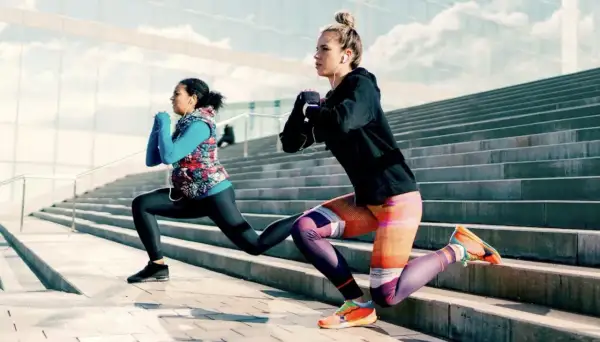 Deux femmes font des fentes sur des escaliers extérieurs, profitant d'une séance de ppg sport sous un ciel bleu.