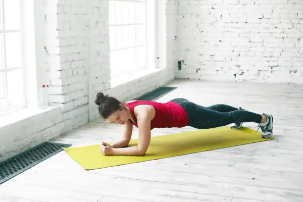 Femme en tenue de sport effectuant la planche sur un tapis jaune, renforçant son corps.