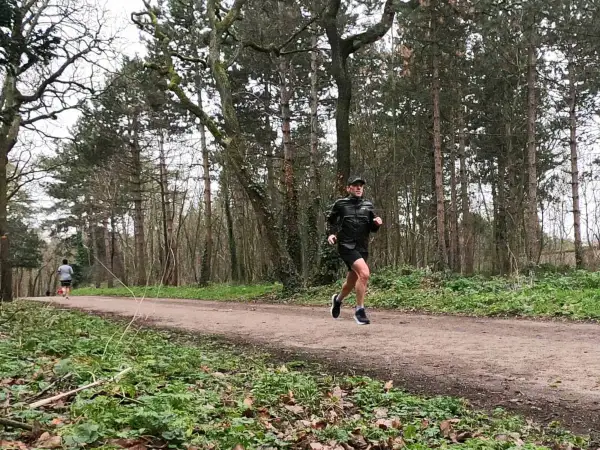 Un homme en tenue de sport ef running sur un sentier forestier, entouré d'arbres.